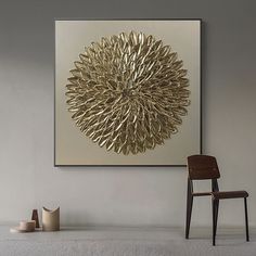 a chair sitting in front of a large gold flower on a wall above a table