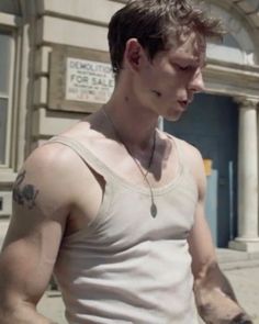 a man with tattoos on his arm walking down the street in front of a building