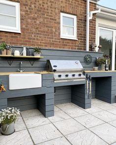 an outdoor kitchen that is built into the side of a brick building with potted plants on it