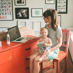 a woman sitting at a desk with a baby on her lap while using a laptop