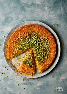 a cake with pistachio on top is cut in half and sits on a plate