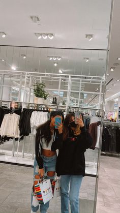 two women are taking pictures in front of a mirror while holding shopping bags and looking at their cell phones