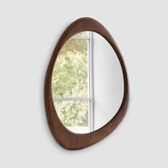 an oval wooden mirror hanging on the wall next to a window with trees in the background