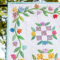 a close up of a quilt hanging on a clothes line with trees in the background