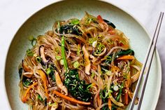 a white plate topped with noodles and veggies next to two chopsticks