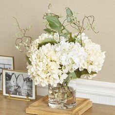 a vase filled with white flowers sitting on top of a wooden table next to pictures