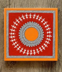 an orange and red box with white designs on the lid sitting on a wooden surface