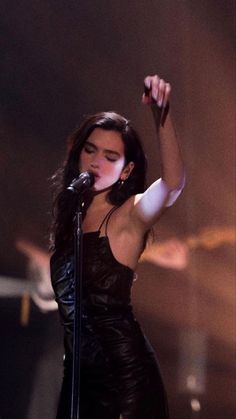 a woman in a black dress holding a microphone up to the side with her right hand