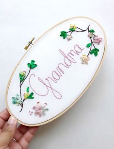 someone is holding up a hand embroidered sign with flowers and the word grandma on it