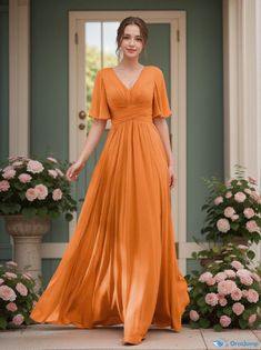 a woman standing in front of a door wearing an orange dress with fluttered sleeves