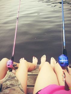 two people are sitting on a dock with fishing rods in their hands and one person is laying down