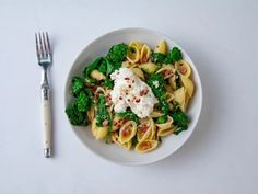 a white plate topped with pasta and broccoli next to a fork on a table