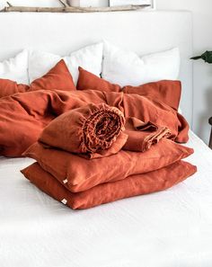 an unmade bed with orange linens and pillows on it in a white bedroom