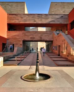 a fountain in the middle of a courtyard with stairs leading up to it and people walking around