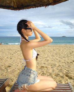 a young woman sitting on top of a wooden bench under an umbrella at the beach