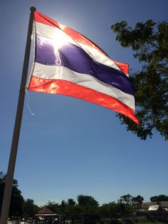 the thai flag is flying high in the blue sky with trees and houses behind it