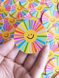 a hand holding a smiley face sticker in front of many colorful circles with smiling faces on them