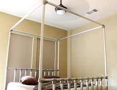 a metal bed frame in a bedroom with beige walls and blinds on the window sill