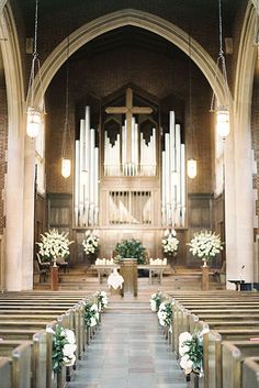 the interior of a church with pews and flowers on the aisle, decorated with greenery