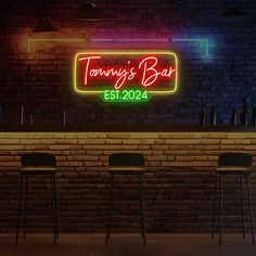 three bar stools in front of a brick wall with a neon sign that says tommy's bar est 2012