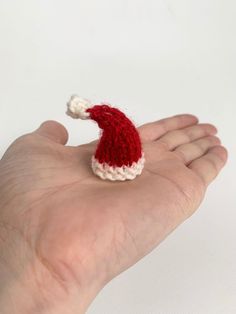 a small red and white knitted santa hat on someone's hand with it's thumb