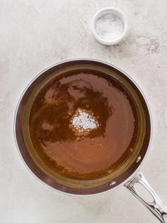 a saucepan filled with brown liquid on top of a white counter next to a spoon