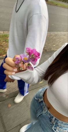 a woman holding flowers in her hands while standing next to a man on the sidewalk