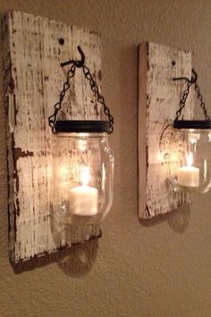 two mason jars are hanging on the wall with candles in them and one candle is lit