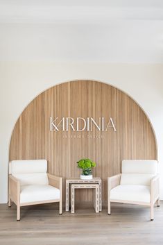 two white chairs sitting next to each other in front of a wall with the name kardinia on it