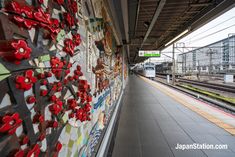 a wall covered in red flowers next to a train station with a train on the tracks