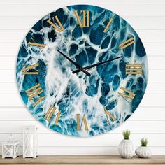 a blue and white clock with gold hands on a wooden table next to a plant