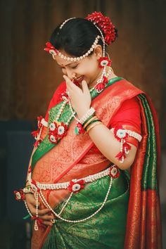 a woman in a green and red sari holding her hand to her face while wearing jewelry