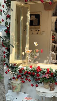 a mirror sitting on the side of a building with red flowers growing out of it