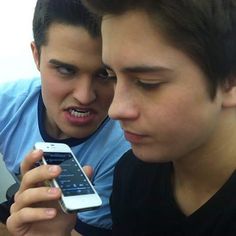 two young men are looking at their cell phones while one looks at the phone screen