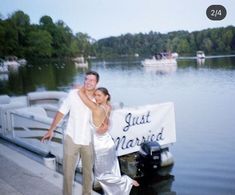 a man and woman standing next to a boat in the water with a just married sign