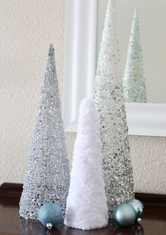 three white and silver christmas trees sitting on top of a wooden table next to a mirror