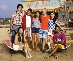 a group of young people standing and sitting on top of a sandy beach