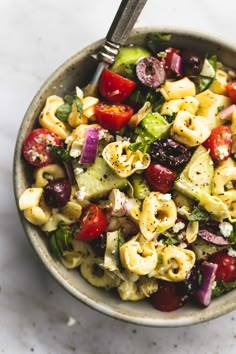 a bowl filled with pasta salad on top of a white countertop next to a fork