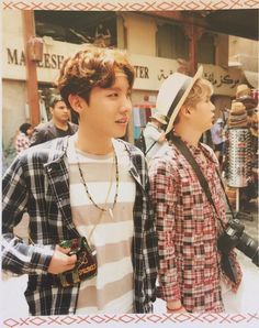 two young men standing next to each other in front of a building with lots of people