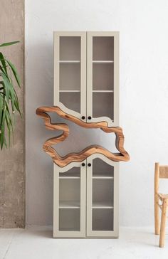 a wooden shelf with two glass doors next to a chair and potted plant on the floor