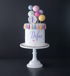 a birthday cake decorated with balloons and confetti on the top is displayed in front of a dark background