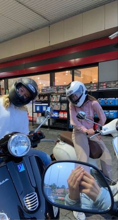 two people on motor scooters in front of a store with their reflection in the side mirror