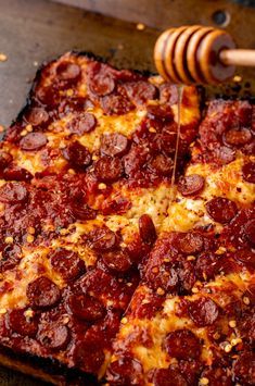 a square pizza with pepperoni and cheese is being cut by a wooden spatula