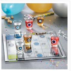 several shot glasses with eyeballs on them sitting on a tray next to balloons and confetti