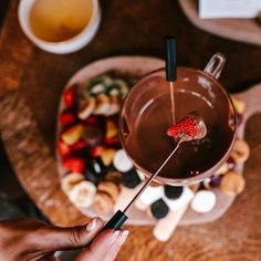 a person is holding a spoon over a chocolate drink with strawberries on the top