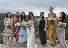 a group of women standing next to each other on top of a hill holding bouquets