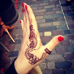 a woman's hand with henna on it and red nail polish holding up her hand