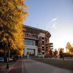 the sun shines on an empty football stadium with trees lining the walkway and parking lot