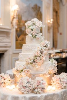 a white wedding cake with flowers on it sitting on a table in front of a fireplace