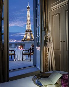 the eiffel tower is seen through an open window in this room with a table and chairs